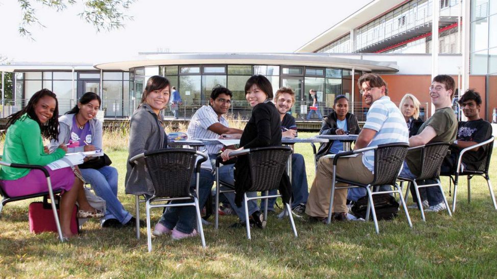 People sittig at a table in front of a building, smiling and turning to the camera